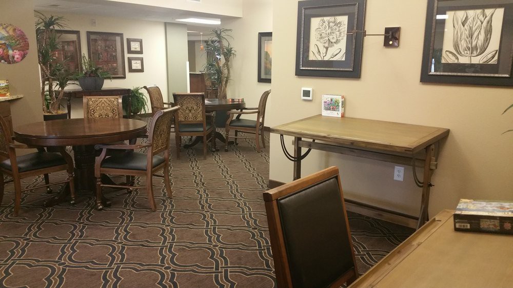 An empty meeting room with neatly arranged tables and chairs, featuring framed artwork on the walls and a patterned carpet.
