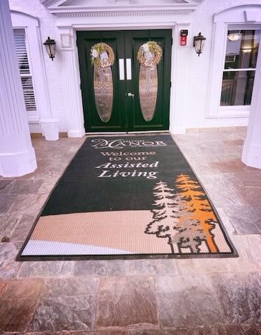 Entrance to a building with an 'Assisted Living' carpet leading to double doors.