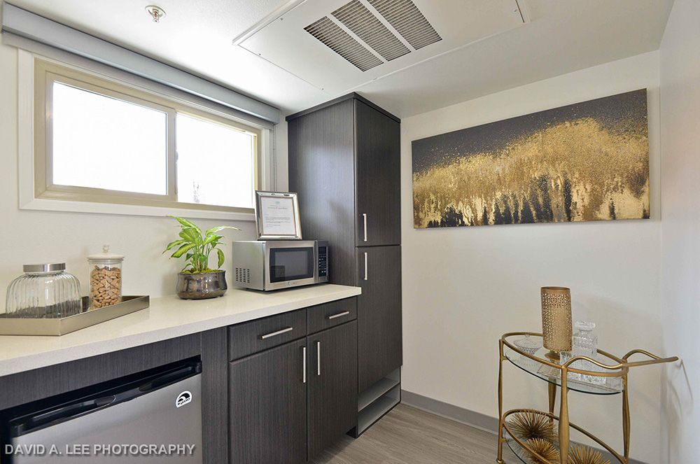 A modern kitchen with sleek dark cabinets, a microwave, and refrigerator, decorated with artwork on the wall.