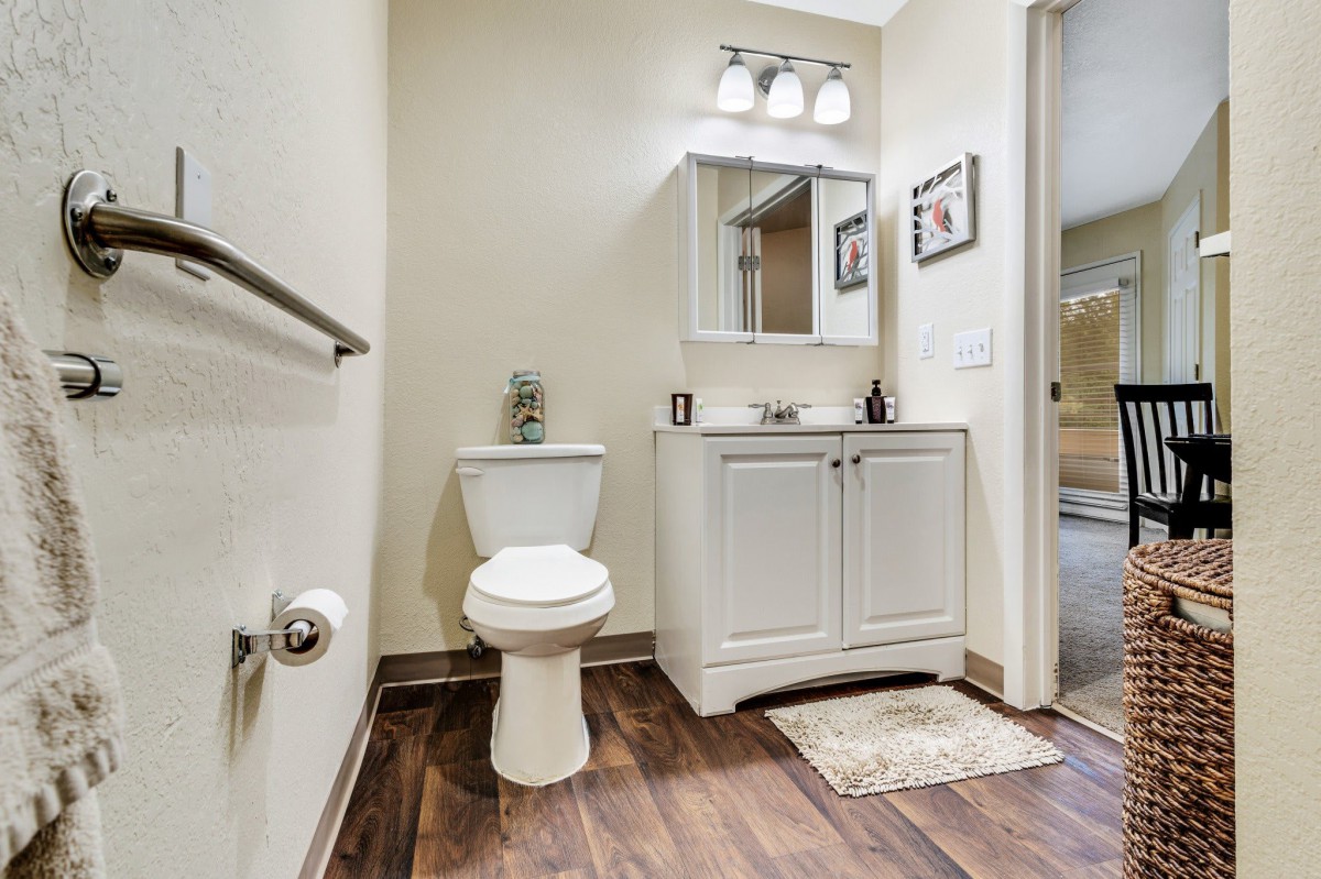 A modern bathroom with a toilet, sink, and vanity cabinet on a hardwood floor.