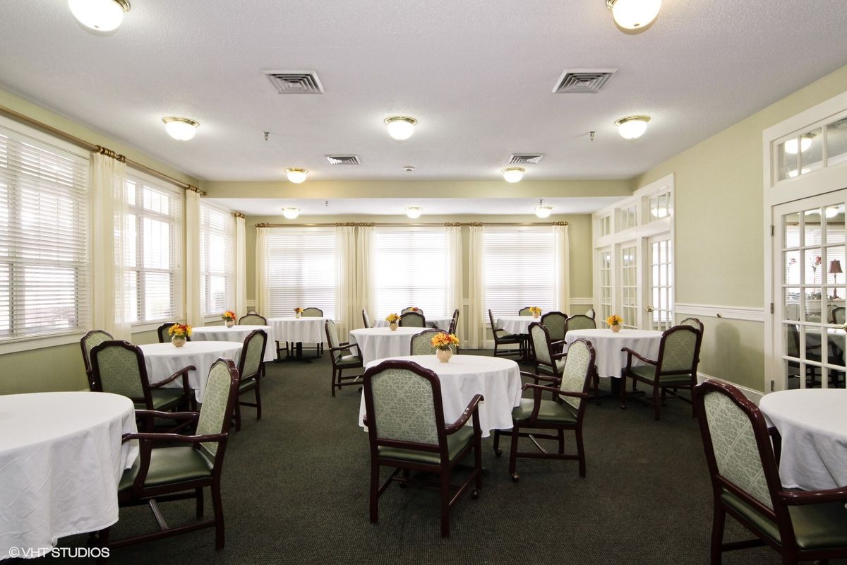 An empty dining room with tables and chairs arranged neatly, illuminated by natural light from large windows.