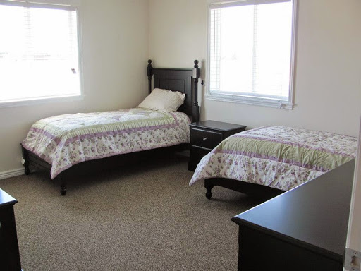 A neatly arranged bedroom featuring two twin beds and a nightstand, illuminated by natural light from the windows.