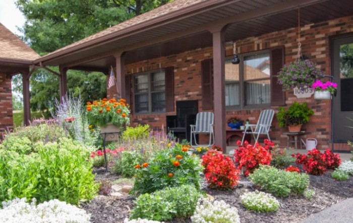 A vibrant garden with blooming flowers and a cozy porch featuring chairs.