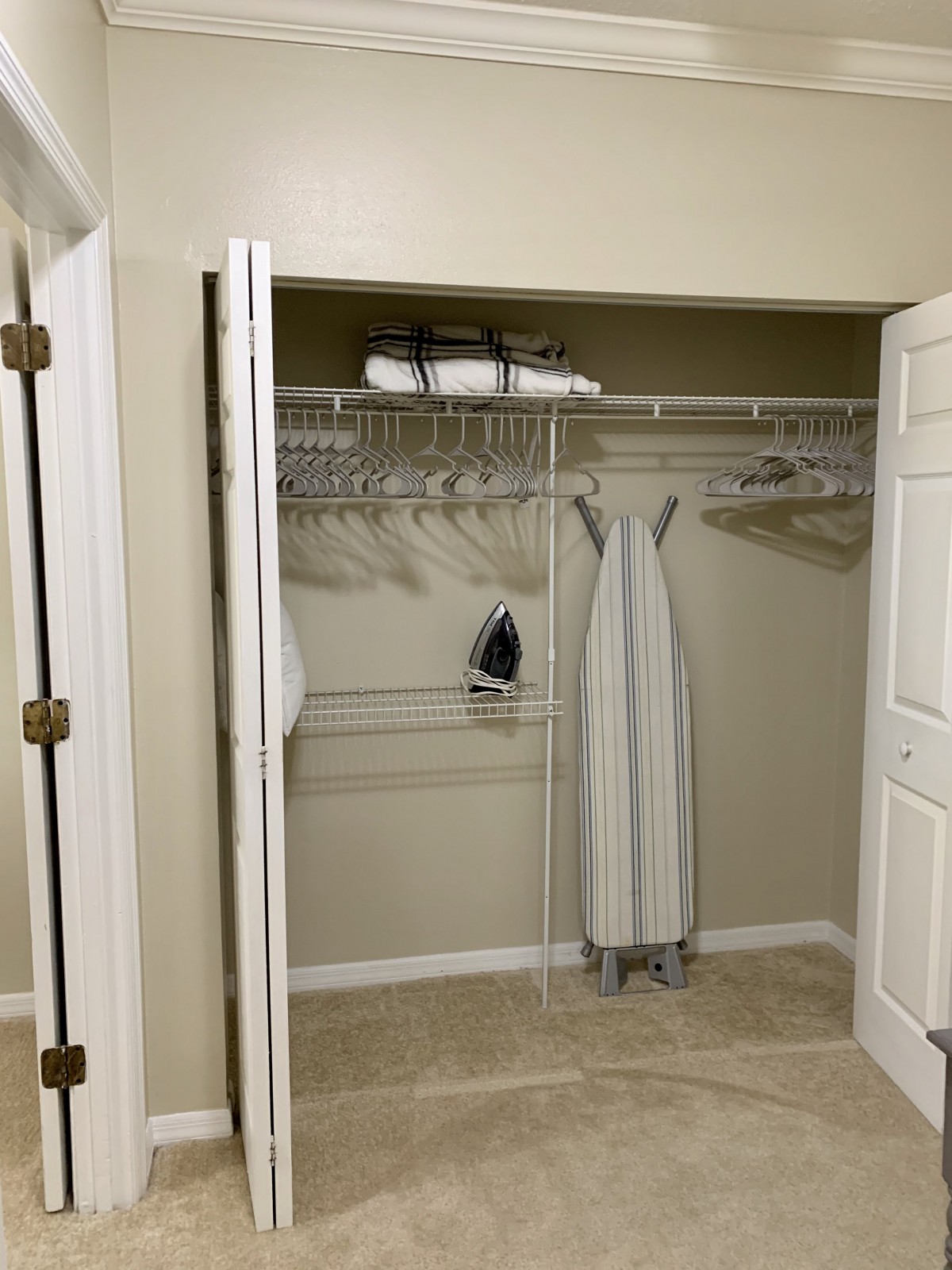 A neatly organized closet featuring an ironing board, iron, towels, and hangers.