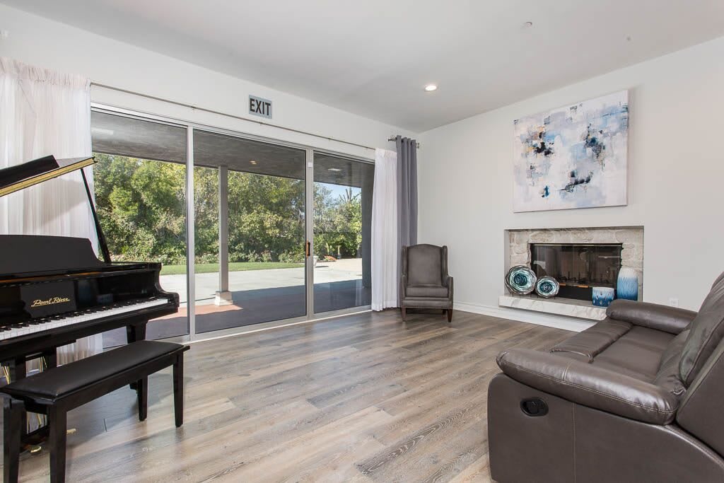 A modern living room featuring a grand piano, a cozy fireplace, and large sliding glass doors leading to a garden.
