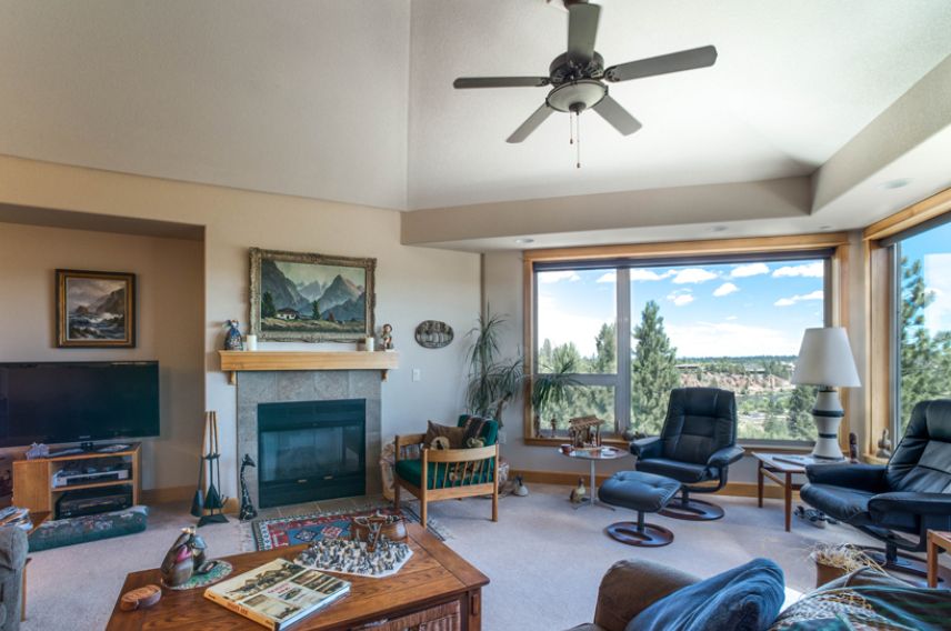 Cozy living room with a fireplace, ceiling fan, and large window offering a scenic view.
