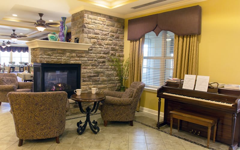 A cozy living room with a stone fireplace, two armchairs, and a piano.