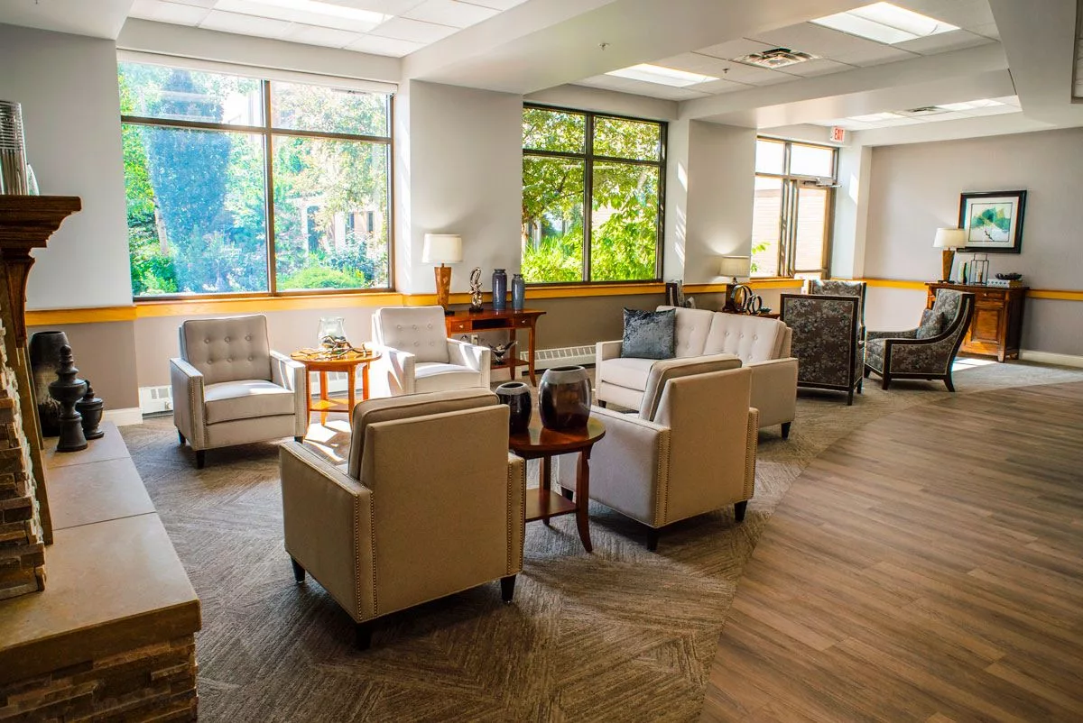 A bright and comfortable waiting room with chairs and tables arranged around large windows.