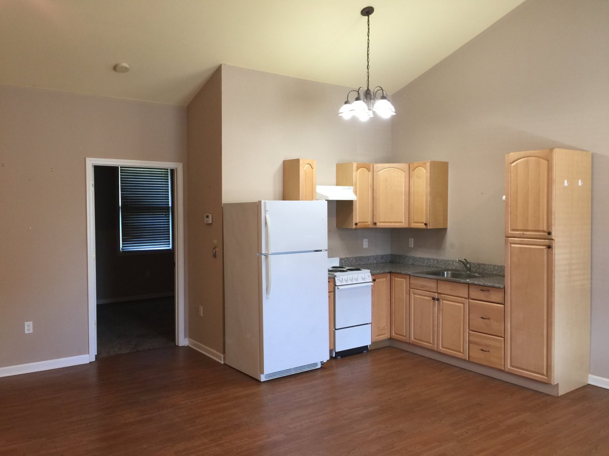 A small kitchen area in an apartment featuring wooden cabinets, a fridge, and a stove.