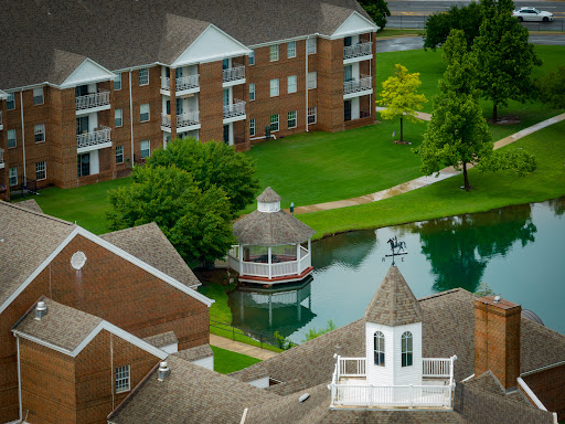 A scenic view of a residential area featuring apartments, a gazebo, and a pond surrounded by lush greenery.