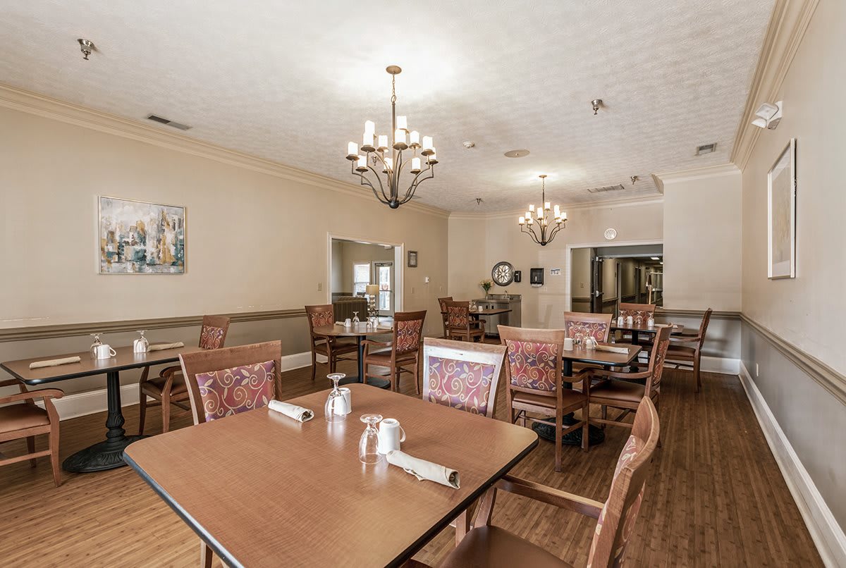 A spacious dining room with elegant chandeliers, neatly arranged tables and chairs, and a warm wooden floor.