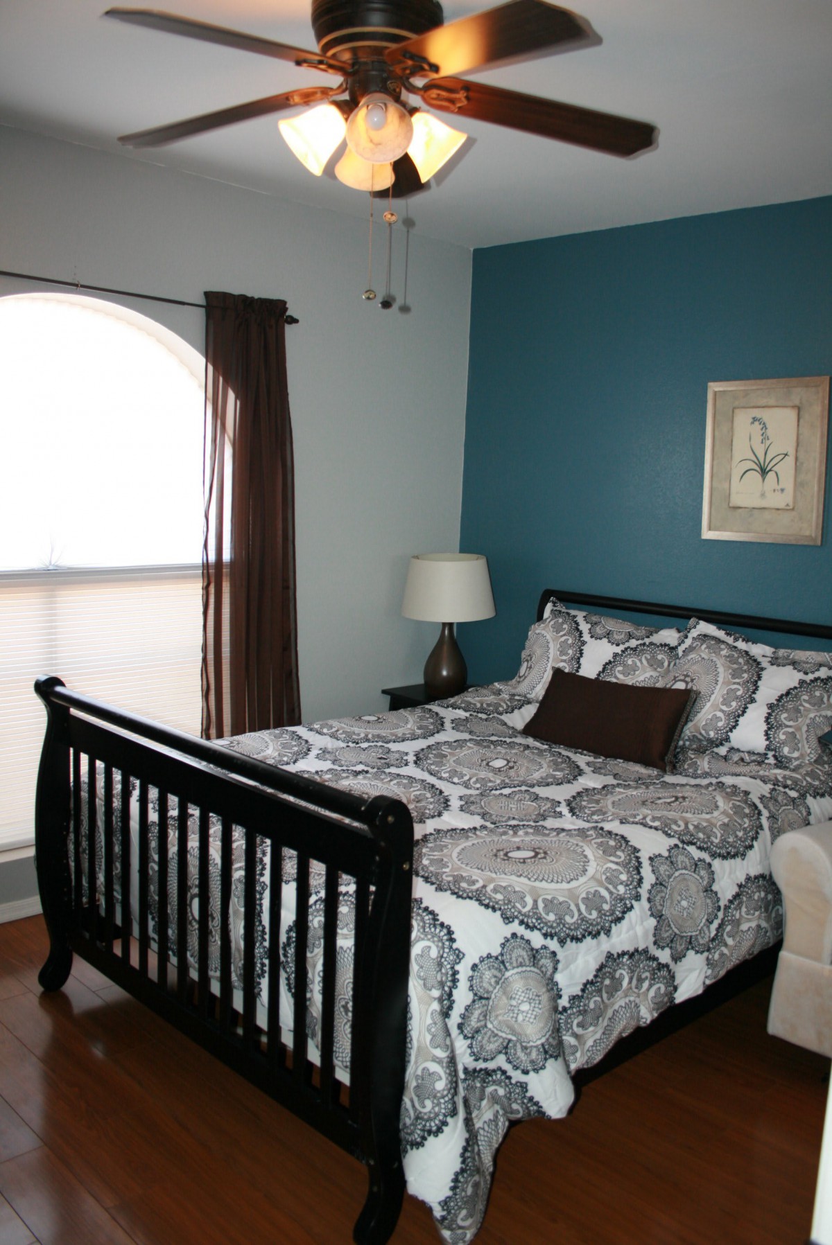 A cozy bedroom with a patterned bedspread, dark wooden bed frame, and a bedside lamp against teal and light blue walls.