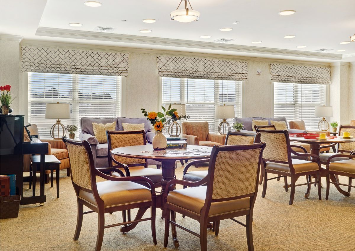 A spacious dining room with round tables and comfortable chairs, featuring large windows and elegant decor.