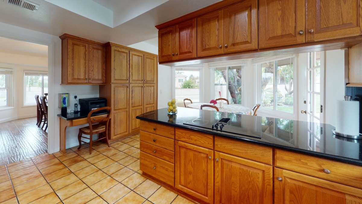 A spacious kitchen with wooden cabinets, a granite countertop island, and large windows letting in natural light.