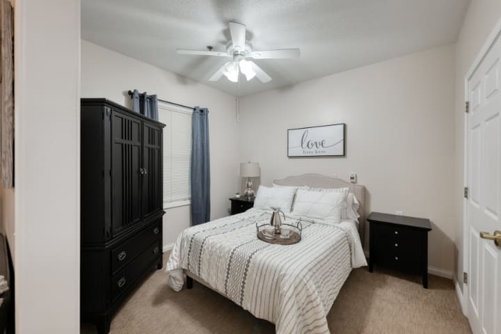 A cozy, minimalistic bedroom featuring a neatly made bed with striped bedding, a wardrobe, nightstands, and a ceiling fan.
