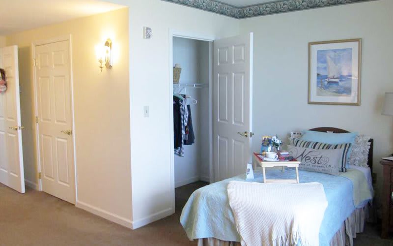 A cozy bedroom with a neatly made bed, adjacent closet, and wall-mounted lamp.