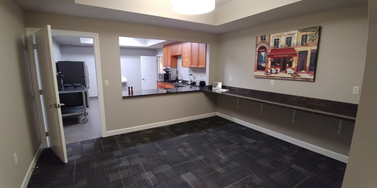 A modern office area with a view into a kitchen, featuring carpet flooring and a countertop workspace.
