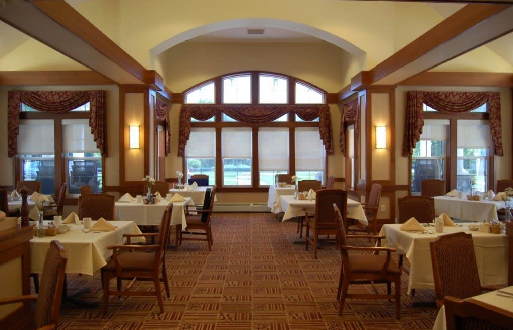 A warmly lit dining room with elegantly set tables and large windows.