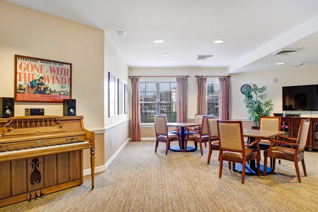 A cozy dining and lounge area featuring a piano, tables, and chairs with large windows allowing natural light.