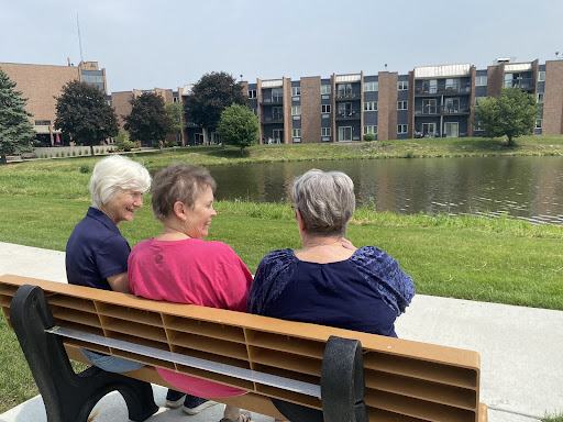 Three women enjoying a peaceful moment together by the water in a park.