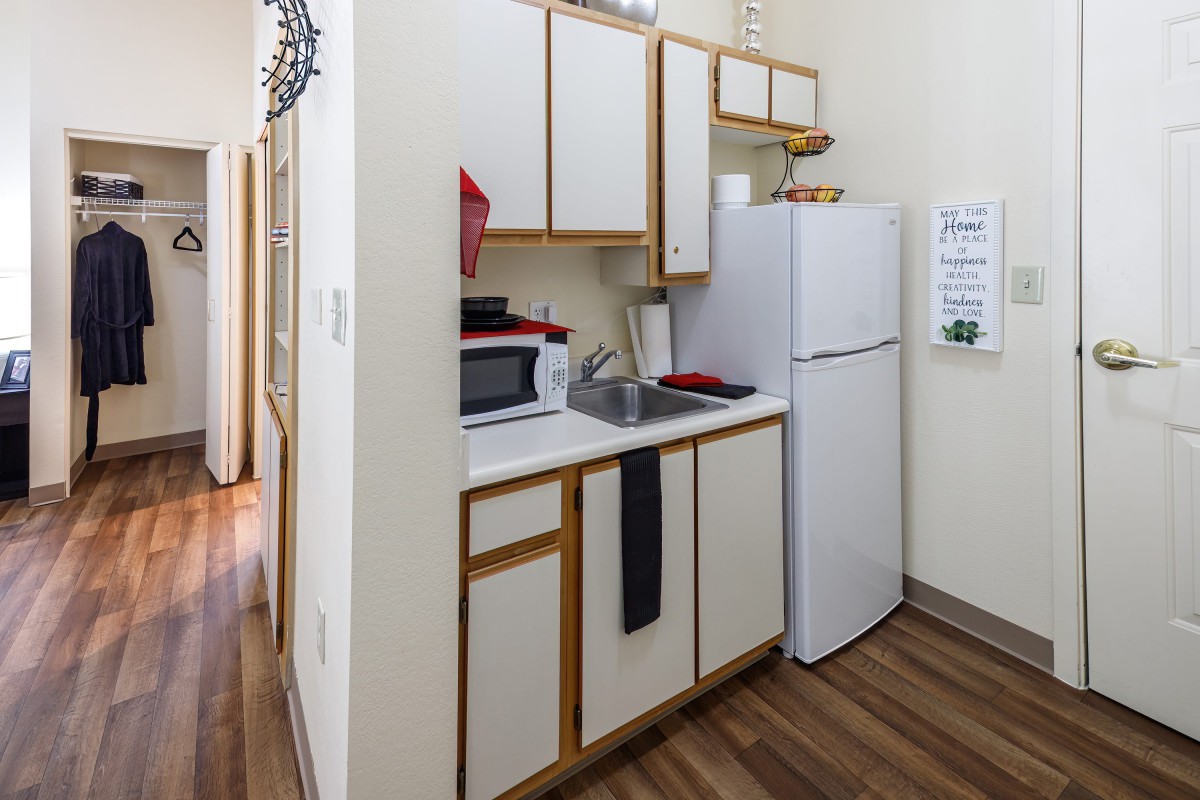 A compact apartment kitchen with essential appliances and wooden flooring.