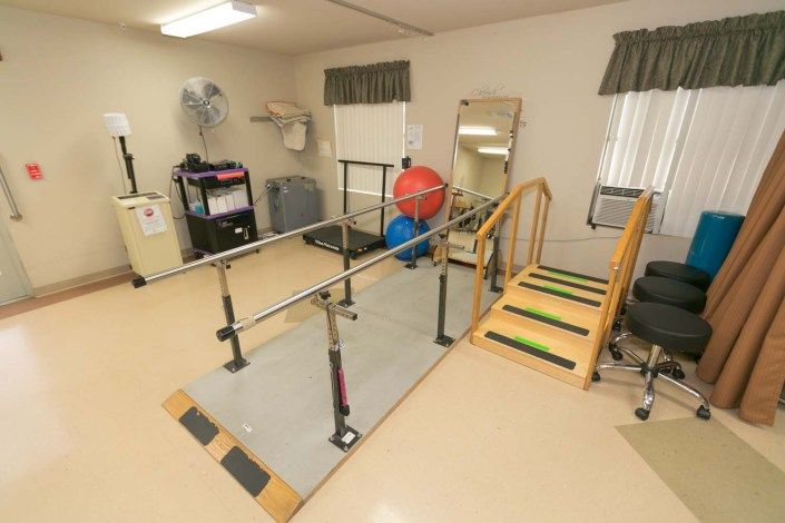A rehabilitation room equipped with parallel bars, a therapy ball, and stairs for physical therapy exercises.