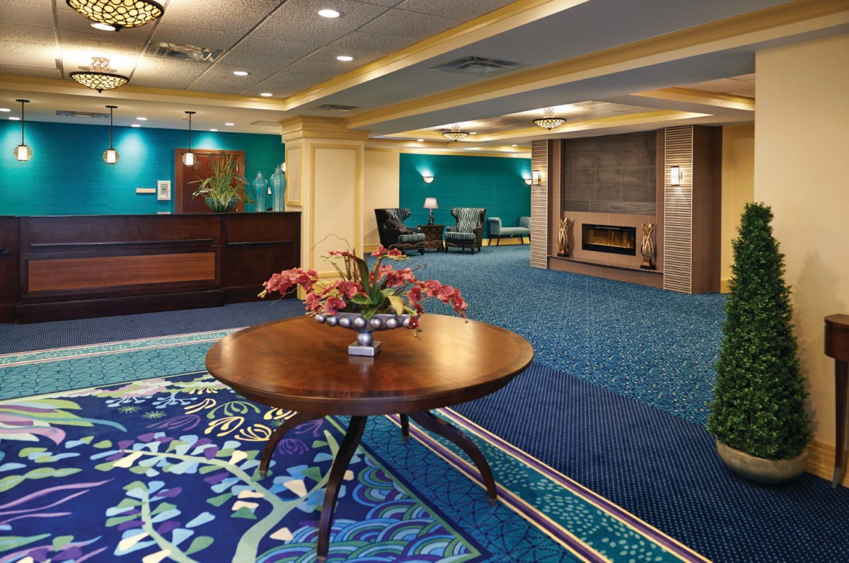 A modern hotel lobby featuring a round table with a floral arrangement, comfortable seating, and a fireplace.