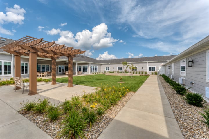 A landscaped courtyard with a pergola and pathways under a blue sky with clouds.