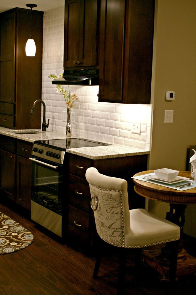 A modern kitchen with dark cabinets and a white backsplash, featuring a small dining area.