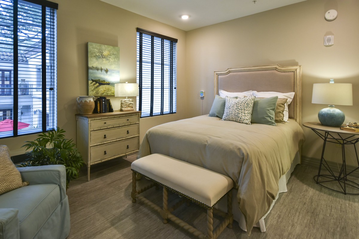 A cozy bedroom with a neatly made bed, nightstand, and soft lighting.