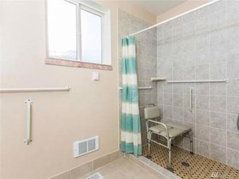 A bathroom featuring a tiled shower with a chair and striped curtain.