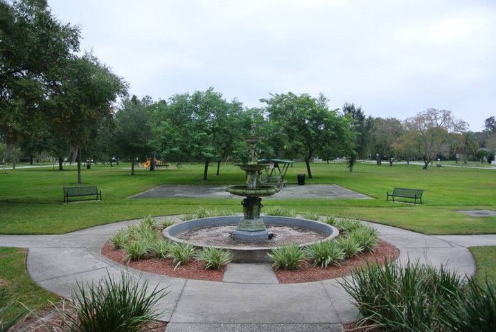 A scenic view of a fountain surrounded by lush greenery and benches in a park.