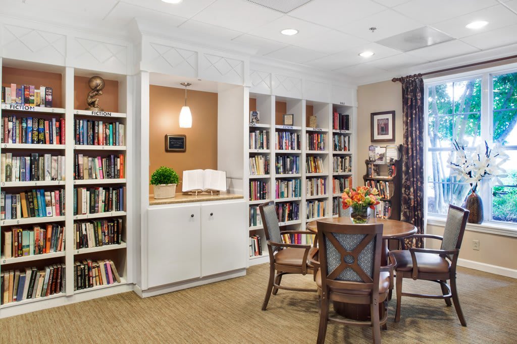 A cozy library corner with bookshelves and a round table surrounded by chairs.