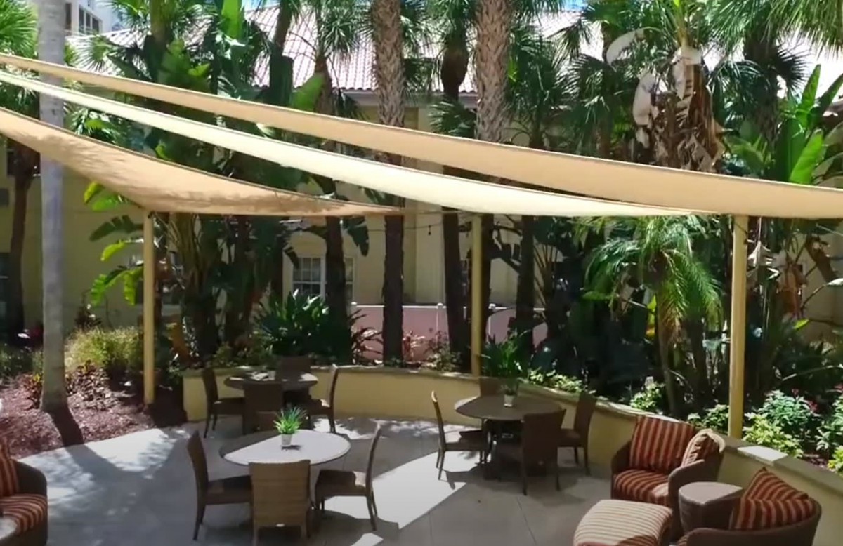 A cozy outdoor patio with seating areas, shaded by sail canopies and surrounded by tropical plants.