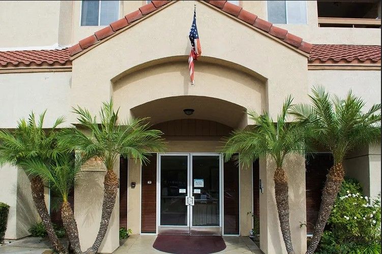 A building entrance with palm trees and an American flag overhead.