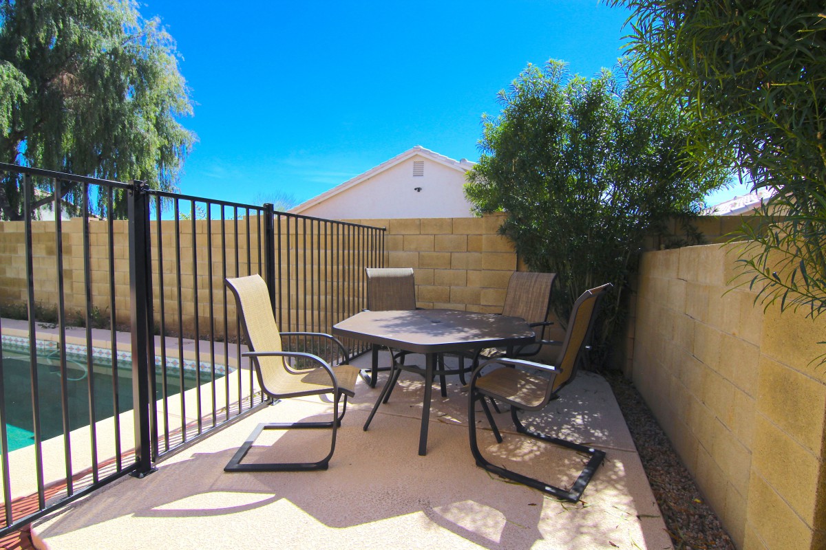 A sunny backyard patio with outdoor furniture and a fenced area.