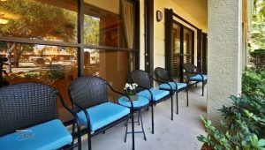 A row of chairs with blue cushions on a patio next to large windows.