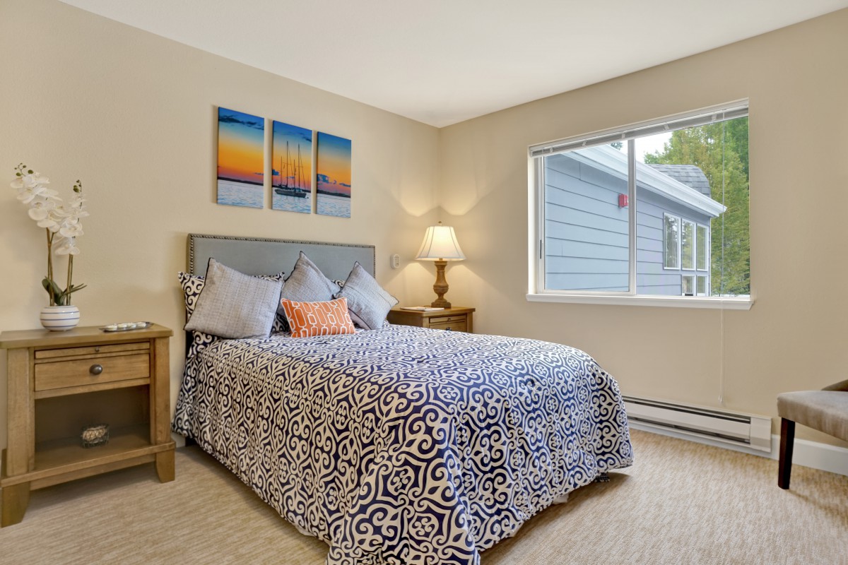 A cozy bedroom with a patterned bedspread, a lamp on the nightstand, and artwork above the bed.