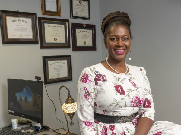 A woman standing in an office with certificates on the wall.