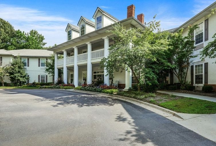 A colonial-style residential building with a large front porch and surrounding greenery.