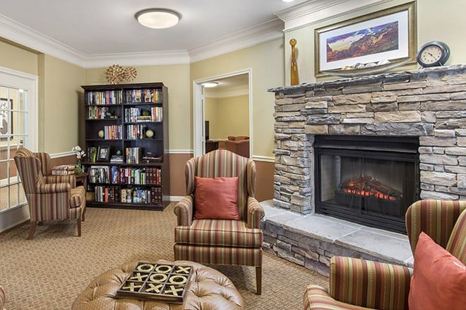 A cozy living room with a stone fireplace, comfortable armchairs, and a bookshelf filled with books.