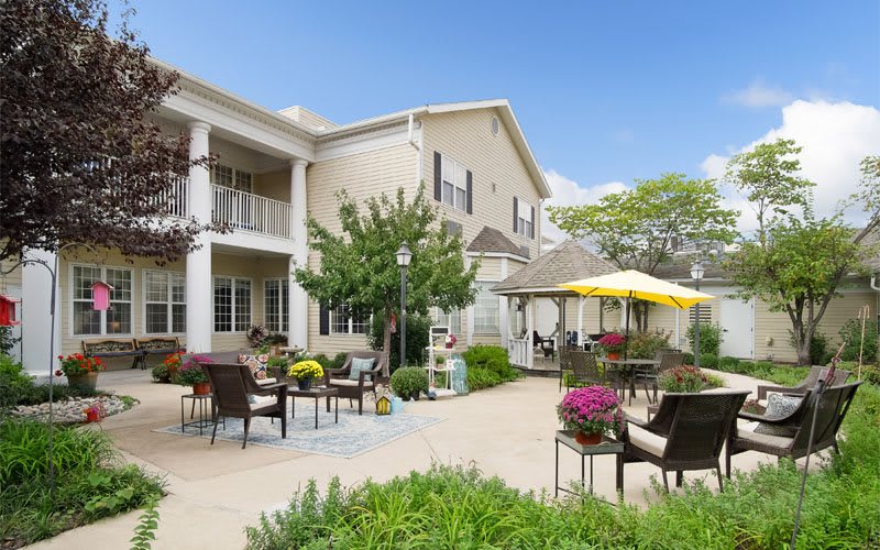 A beautifully landscaped patio area with outdoor furniture and vibrant flowers, adjacent to a residential building.
