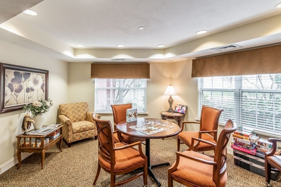 A cozy living area featuring a round table with four chairs, an armchair, a lamp, and large windows.