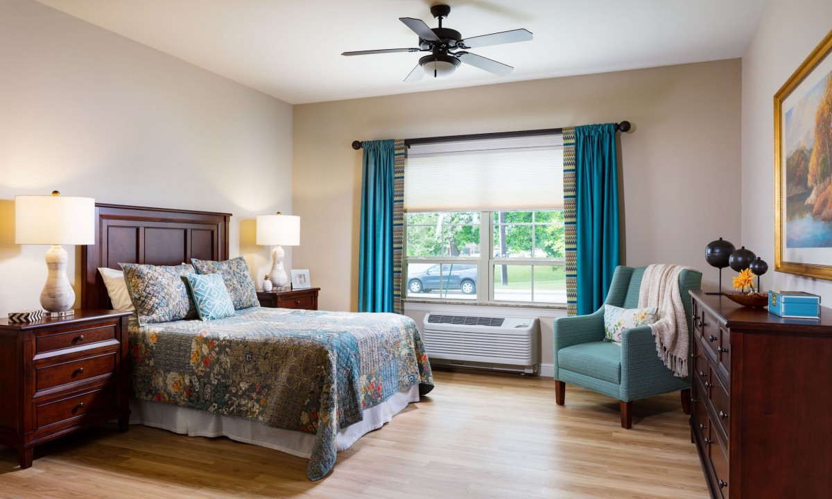 A cozy bedroom with a king-sized bed, teal curtains, and a comfortable armchair.