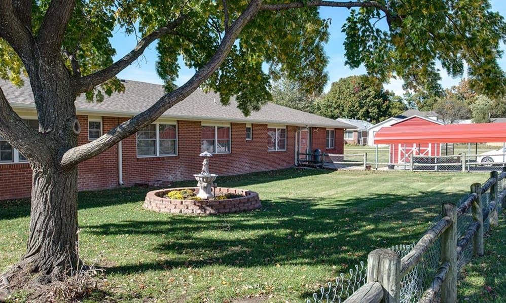 A brick house with a well-maintained lawn, featuring a tree and a fountain in the front yard.