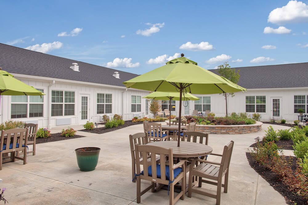 A courtyard featuring a wooden table set with green umbrellas against a backdrop of a white building and blue sky.