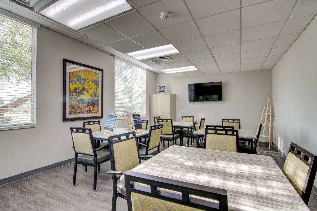 A bright and modern classroom or conference room equipped with tables, chairs, a TV, and wall artwork.