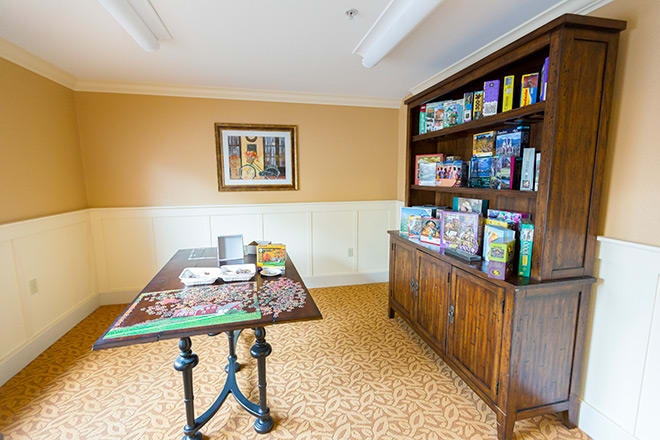 A cozy puzzle room featuring a table with an ongoing jigsaw puzzle and a bookcase filled with board games and puzzles.