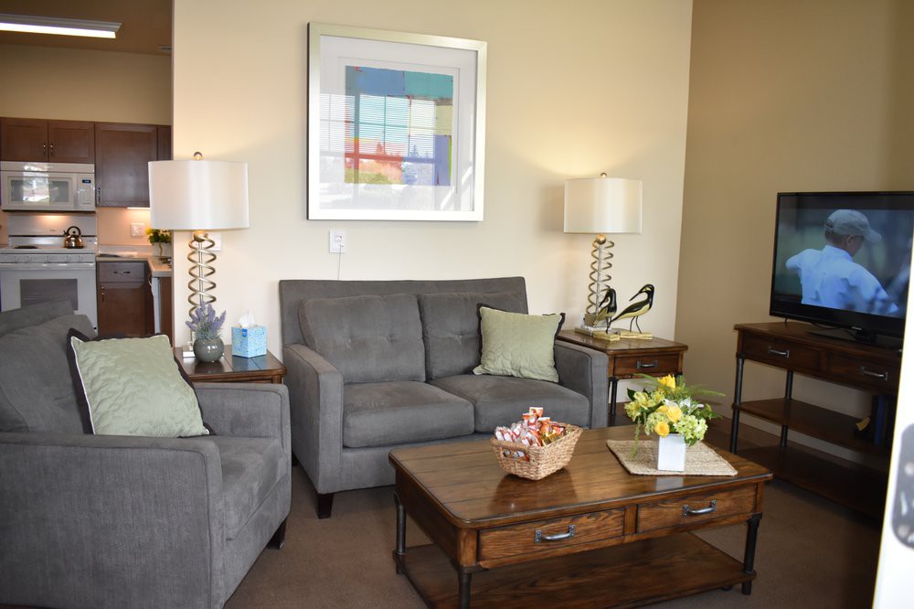 A cozy living room with a gray sofa, wooden coffee table, and stylish lamps on either side. A colorful piece of artwork hangs on the wall above the sofa.