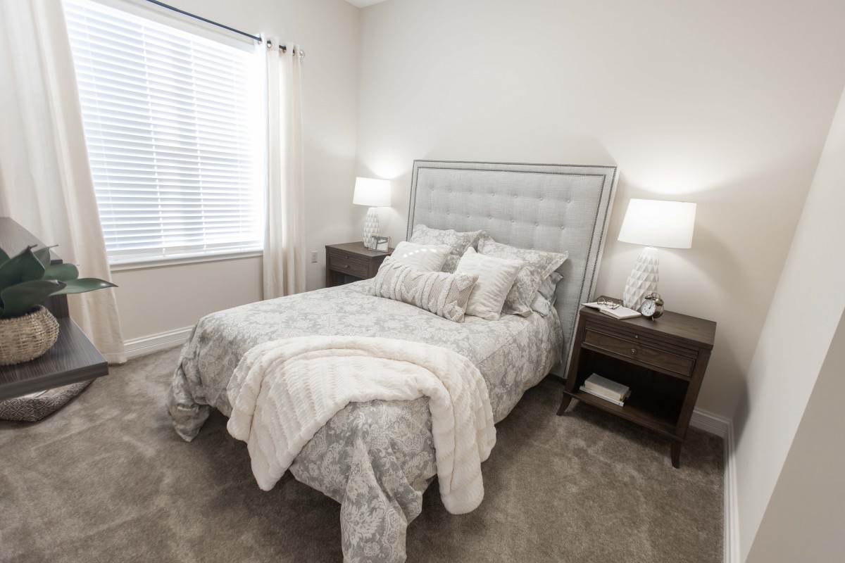 A cozy bedroom with a neatly made bed, two nightstands, modern lamps, and soft carpet.